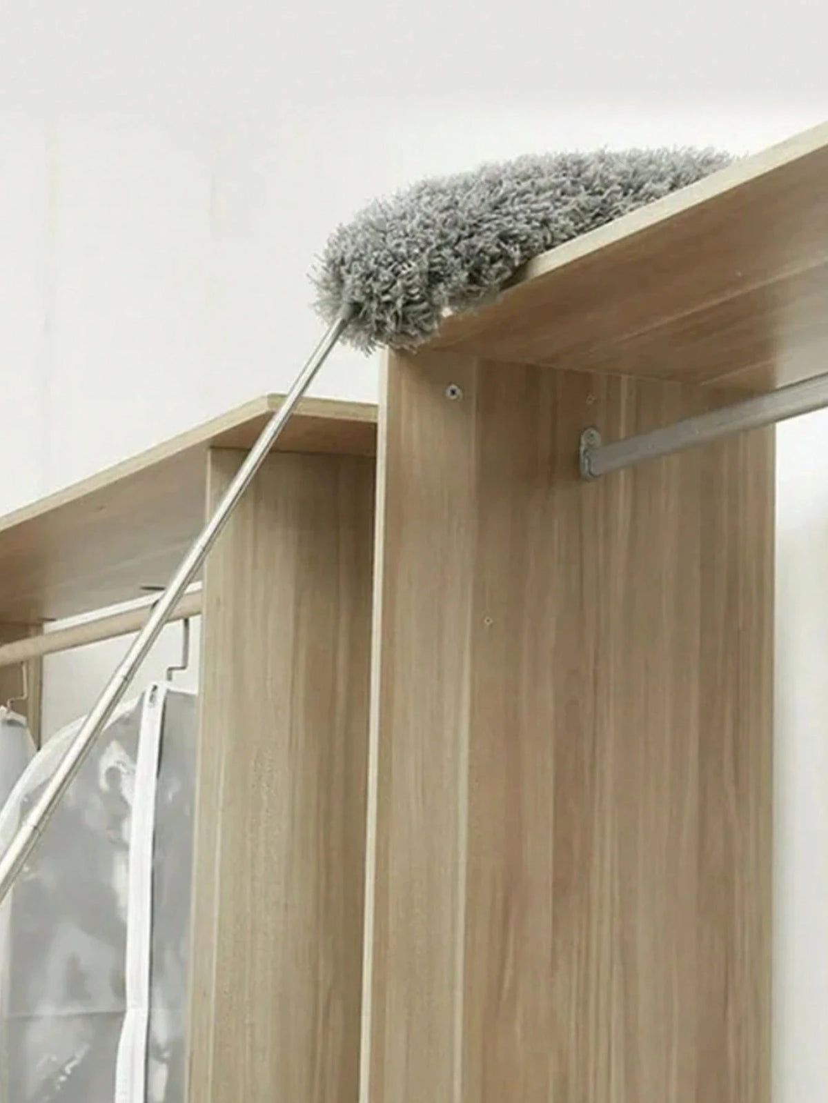 A flexible microfiber duster with a grey fuzzy head is shown resting on a wooden cabinet shelf.