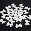 A pile of 100 white acrylic pearl spacer beads shaped like bows for jewelry making