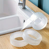 Clear reusable double-sided adhesive tape rolls placed on a wooden surface next to a white sink.
