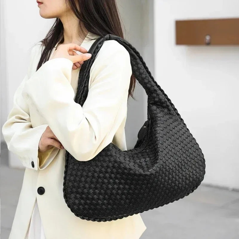 A woman holds a black woven vegan leather hobo bag against a light colored coat.