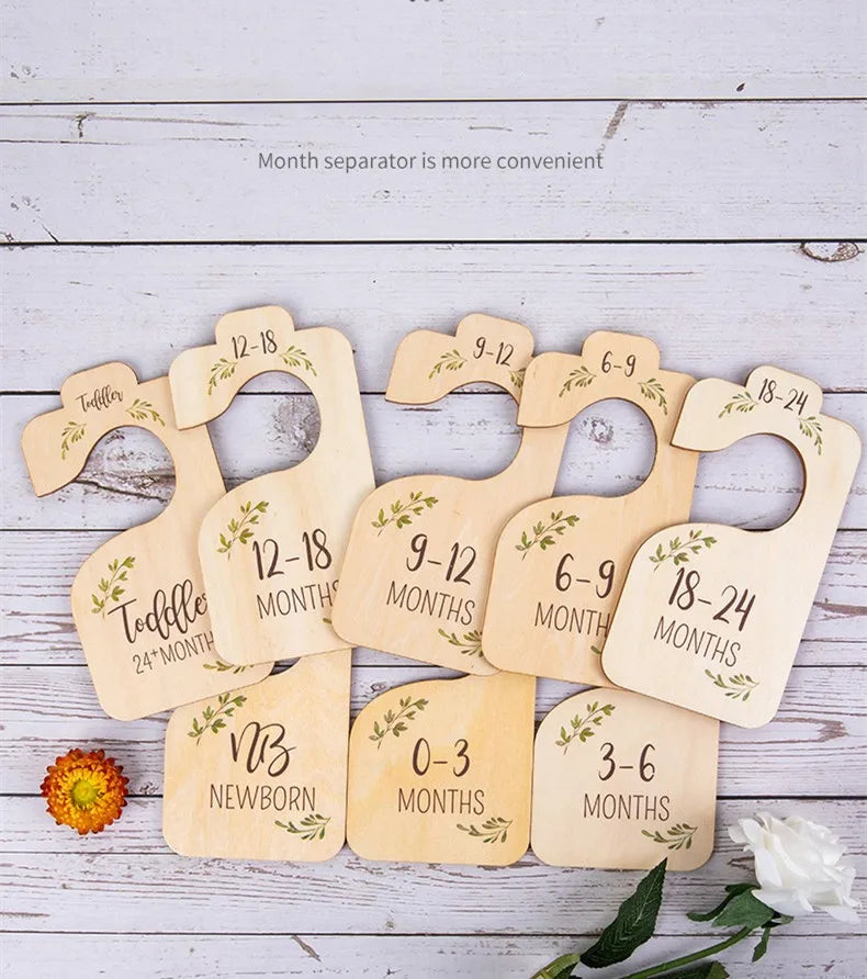 A set of eight wooden baby closet dividers labeled with months, ranging from newborn to 24 months, displayed on a white woode