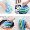 A hand is using a blue and yellow sponge cleaning brush to clean a sink and a frying pan.