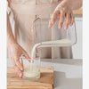 A hand pours white yogurt from a stainless steel strainer into a glass on a wooden board.