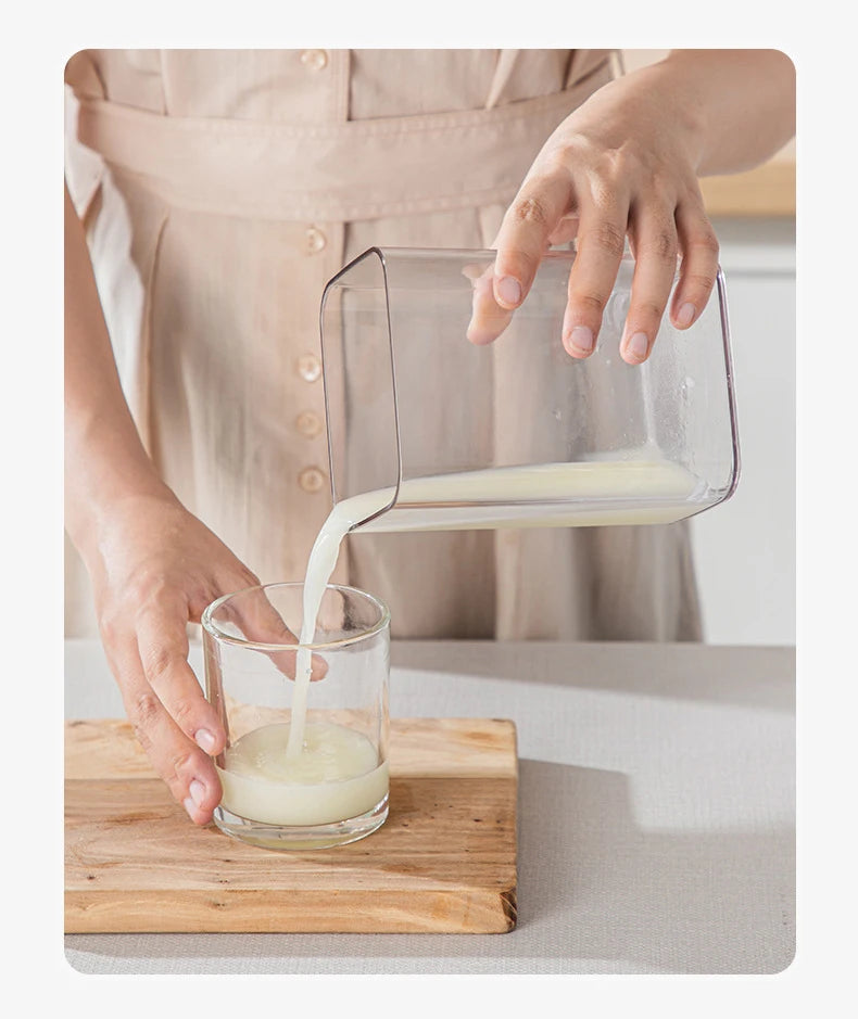 A hand pours white yogurt from a stainless steel strainer into a glass on a wooden board.