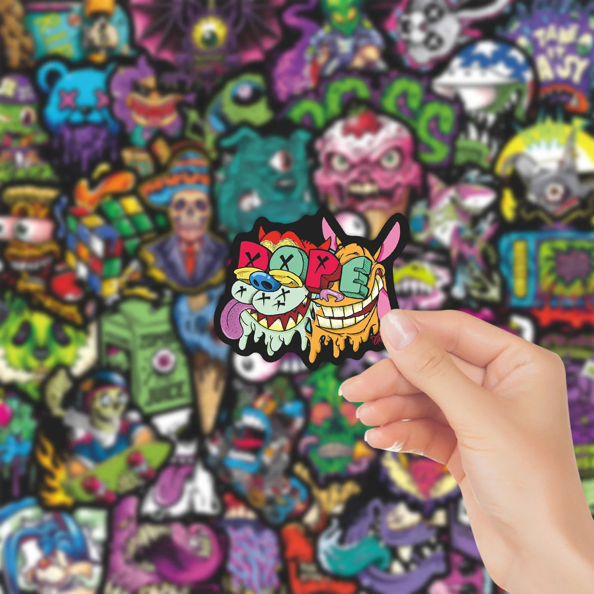 A hand holds a black skull sticker featuring colorful eyes and teeth against a background of dense, colorful, stylized skulls
