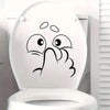 A white toilet lid features a black sticker depicting an expressive, surprised face.