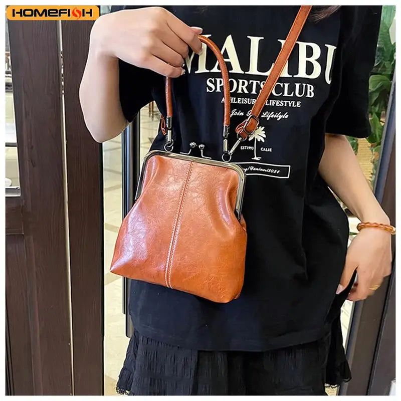 A woman holds a vintage brown PU leather crossbody handbag against a black t-shirt.