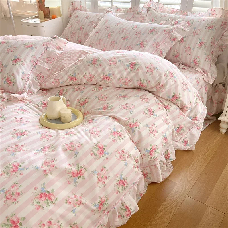 A set of floral ruffle cotton duvet covers in pink and white stripes and floral patterns displayed on a bed.