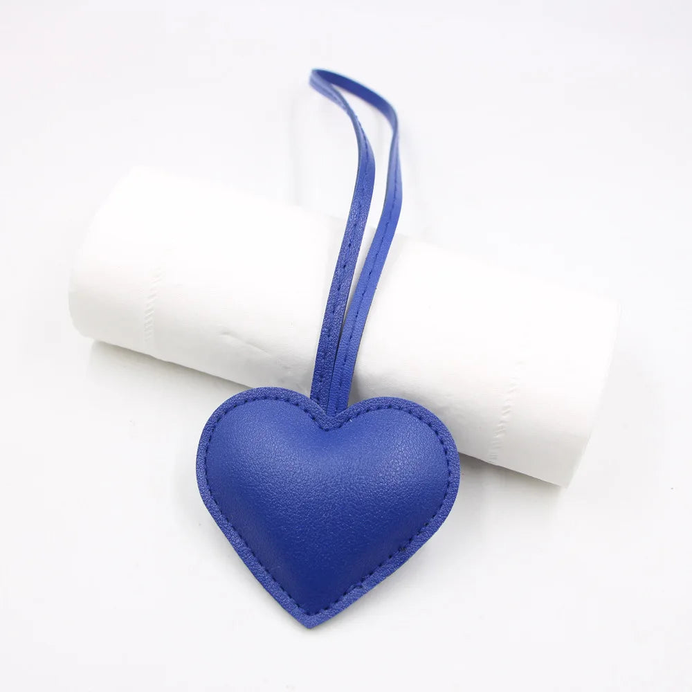 A blue heart-shaped PU leather keychain with a thin cotton peach charm resting on a white rolled object.
