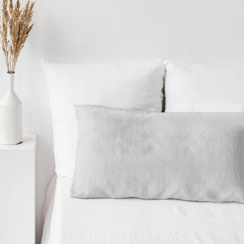 A white linen pillowcase with an envelope closure resting on a white bed.