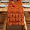 Orange textured table runner with pumpkin patterns set on a wooden table for autumn holiday dining