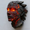 A dark, cracked stone sculpture of a face glowing with intense orange light.