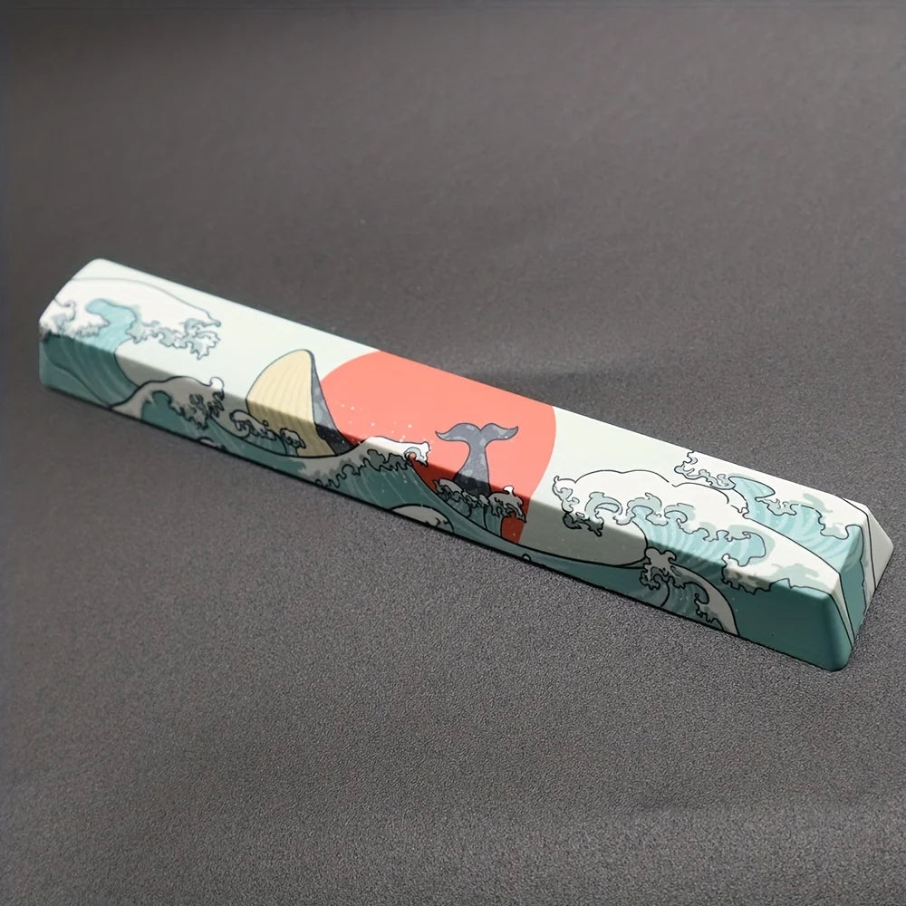 A rectangular light blue keycap featuring a stylized landscape with mountains, waves, and a red sun.