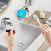 A hand is using a long, thin cleaning brush to clean the faucet of a white sink.