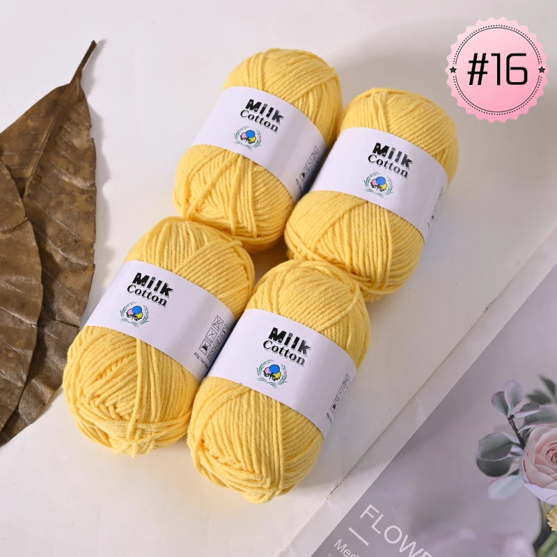 A bundle of yellow Milk Cotton yarn skeins with white labels, displayed next to a dried leaf.