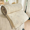 A cream-colored quilt with a pastoral print featuring small animal figures rolled up on a white surface.