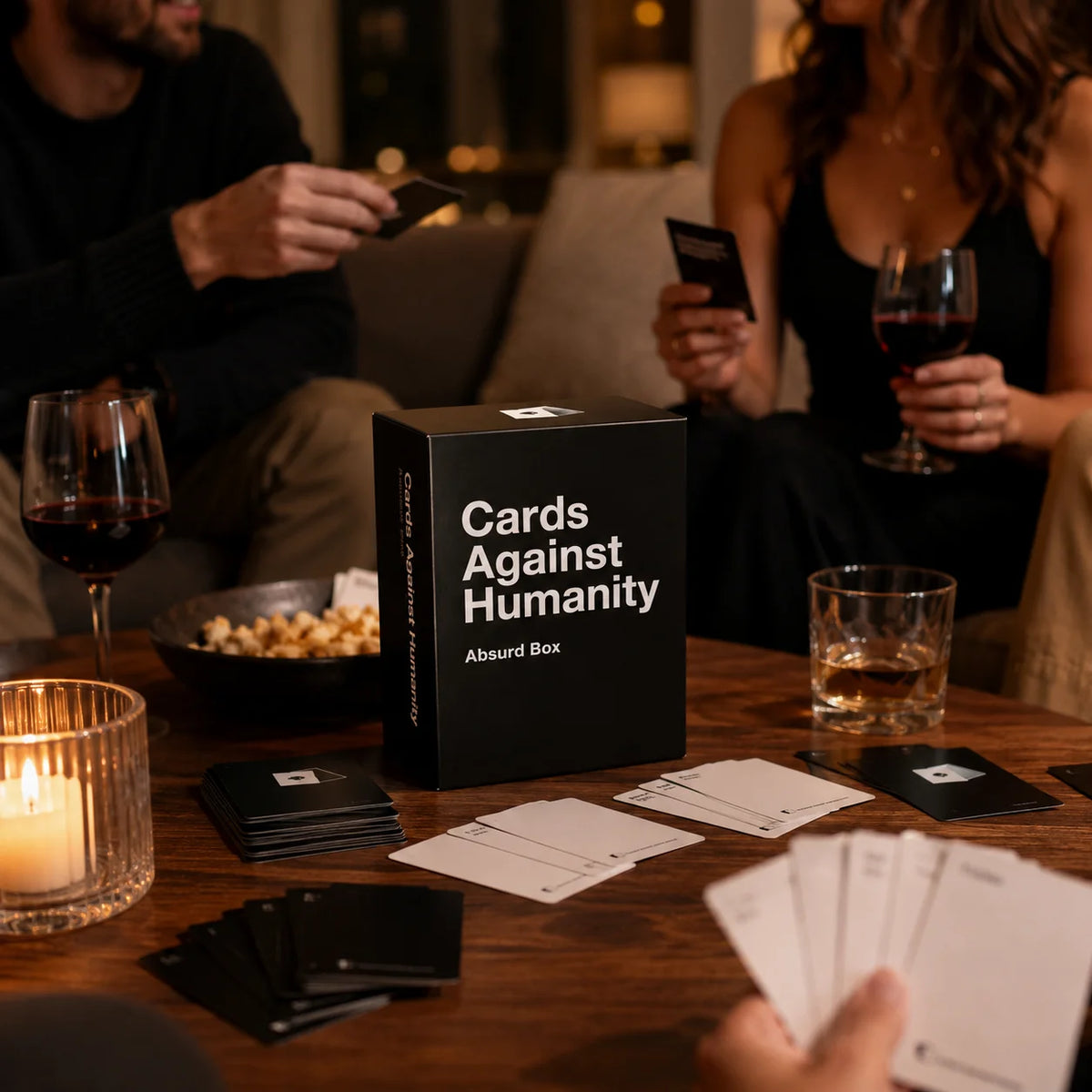 A close-up of a table with cards and glasses, showing people interacting with the Absurd Box party game.