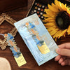 A vintage metal bookmark with an artistic hollow design and tassel rests on a wooden surface next to a sunflower.