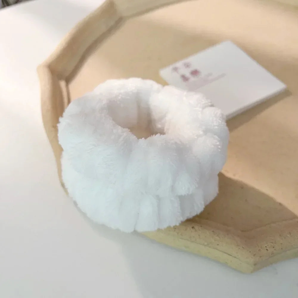 A white microfiber wrist sweatband and scrunchies for face washing resting on a light wooden tray.