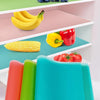 A set of four colorful, flexible EVA fridge shelf liners in orange, lime green, and cyan are displayed on a pink shelf.