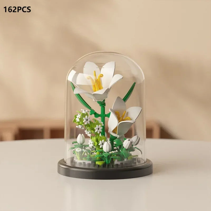 A clear glass dome display featuring a miniature white flower arrangement made of building blocks.