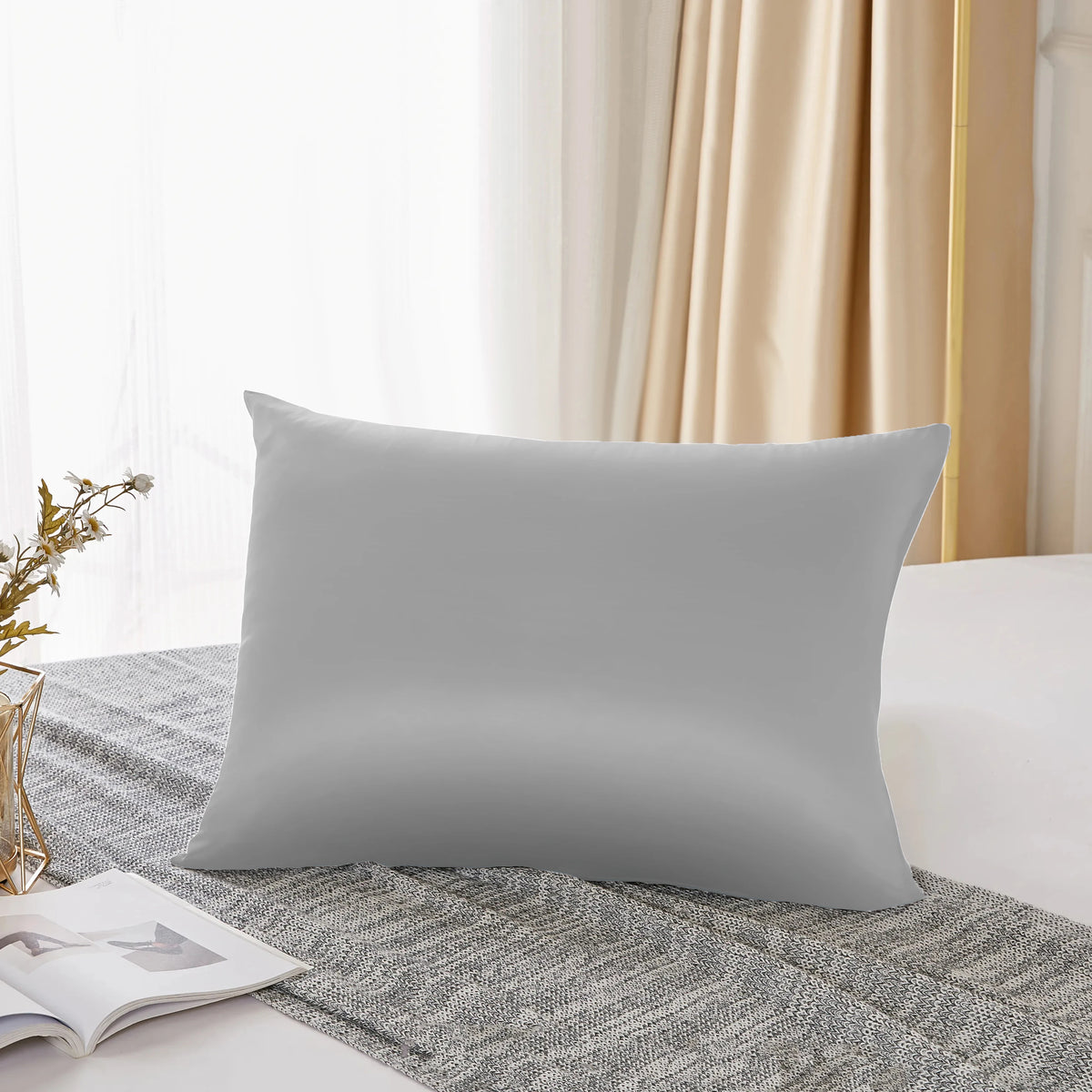 Housse de couette en soie mulberry naturelle gris clair posée sur un tissu gris texturé près d'une fenêtre.