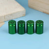 A set of four green bullet shell tire valve stem caps resting on a light blue surface next to a wooden block.