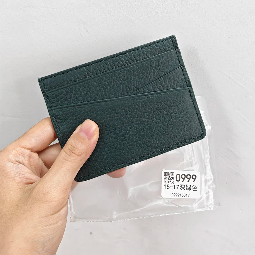 A hand holds a dark green genuine leather slim card holder wallet with a clear plastic packaging.