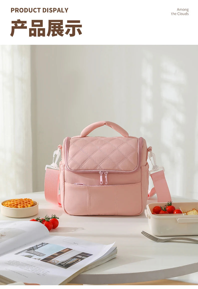 A pink quilted insulated lunch bag is displayed on a white table next to some fresh fruit and an open book.
