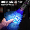 A hand holds a stack of US dollar bills under the beam of a 365nm UV LED flashlight.
