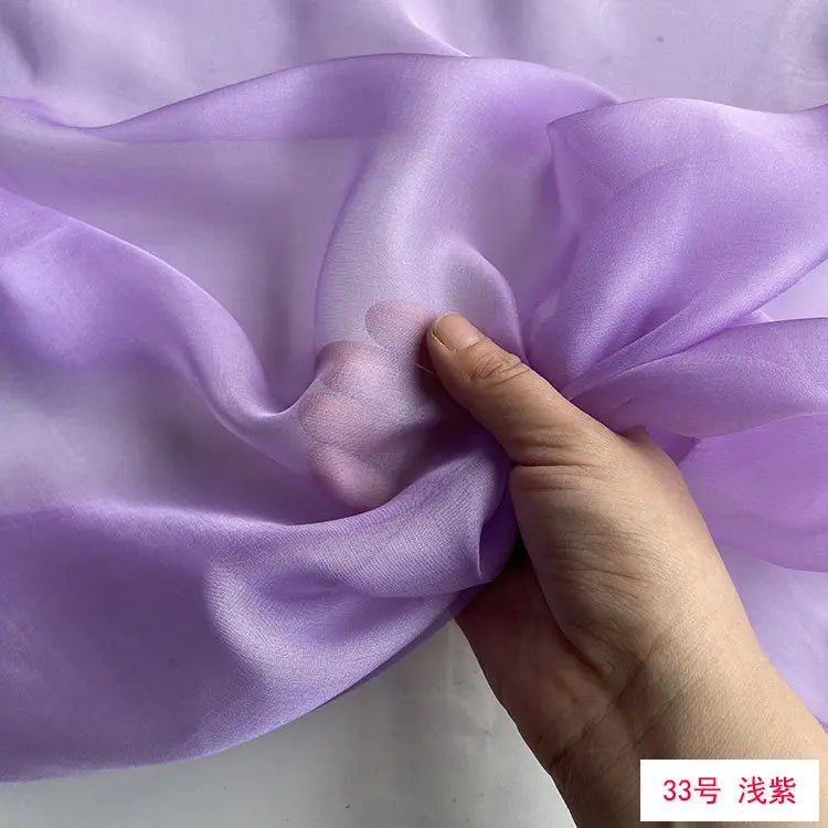 A hand is gently folding a piece of light purple silk chiffon fabric.