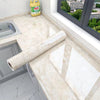 Roll of marble peel-and-stick film displayed on a kitchen countertop with a window view.