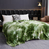 A green and white tie-dye flannel fleece throw blanket draped over a bed.