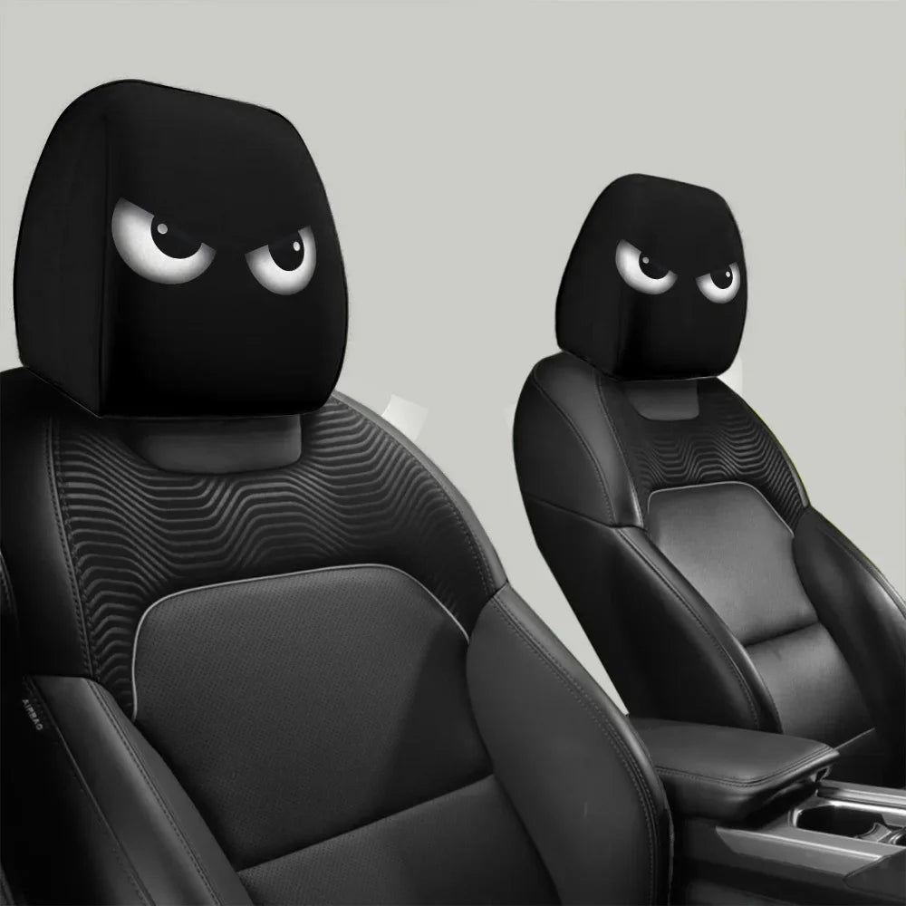 A pair of black car headrest covers with slanted eyes are shown in a vehicle interior setting.