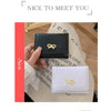 A close-up of a black tri-fold wallet with a gold bow detail next to a white version.