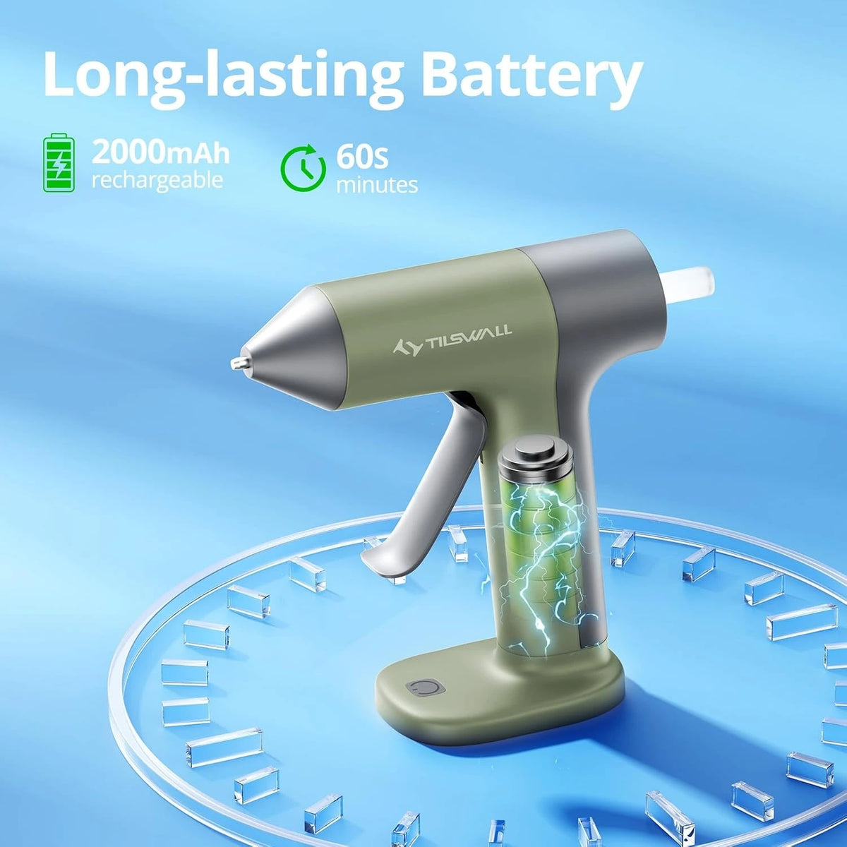 A silver and olive green cordless hot glue gun with a glowing blue nozzle rests on a circular surface.