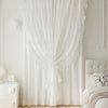 White sheer curtain with ruffled lace detailing hanging in a light-colored room.