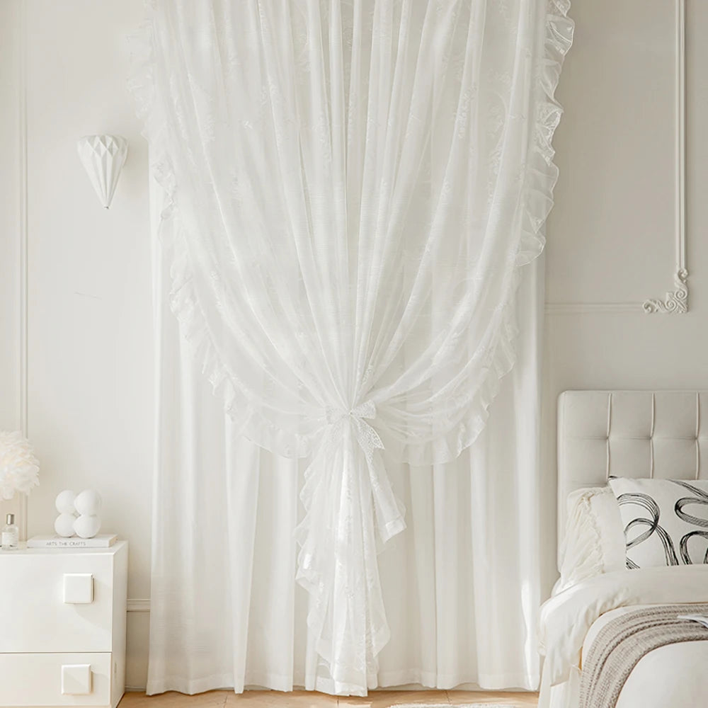 White sheer curtain with ruffled lace detailing hanging in a light-colored room.