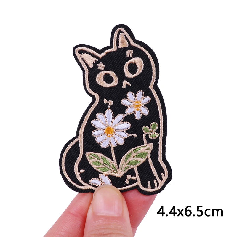 Black embroidery patch of a cat face with white flowers and green leaves