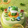 A green frog toy is featured on a tiered platform surrounded by other frogs and a fishing net.