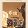 A brown leopard print clutch bag is displayed against a warm, earthy background with flowing gold fabric.