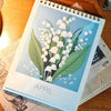 A close-up of a Bloomy Flower desk calendar showing an April illustration of white blossoms on green leaves.