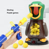 A hand is holding a blue dart gun aimed at a green duck target, with yellow darts scattered nearby.