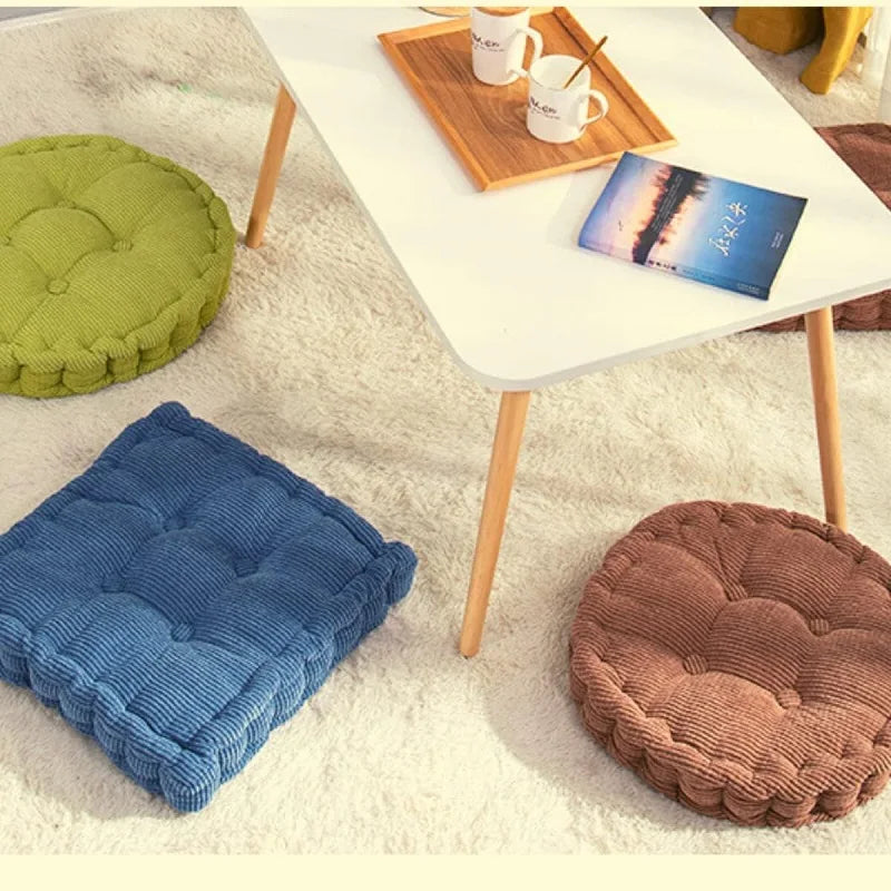 A collection of thick corduroy floor cushions in various shades of green, blue, and brown placed on a white table.