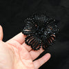 A hand holds a black crystal rhinestone flower sew-on patch for clothing and accessories.