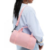 A woman is shown from the back carrying a pink compact nylon gym bag with an adjustable strap over her shoulder.