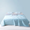 Light blue ice silk cooling blanket folded on a bed with a light purple sheet.
