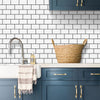 A kitchen backsplash featuring white subway tiles, a sink, and dark blue cabinetry with gold hardware.
