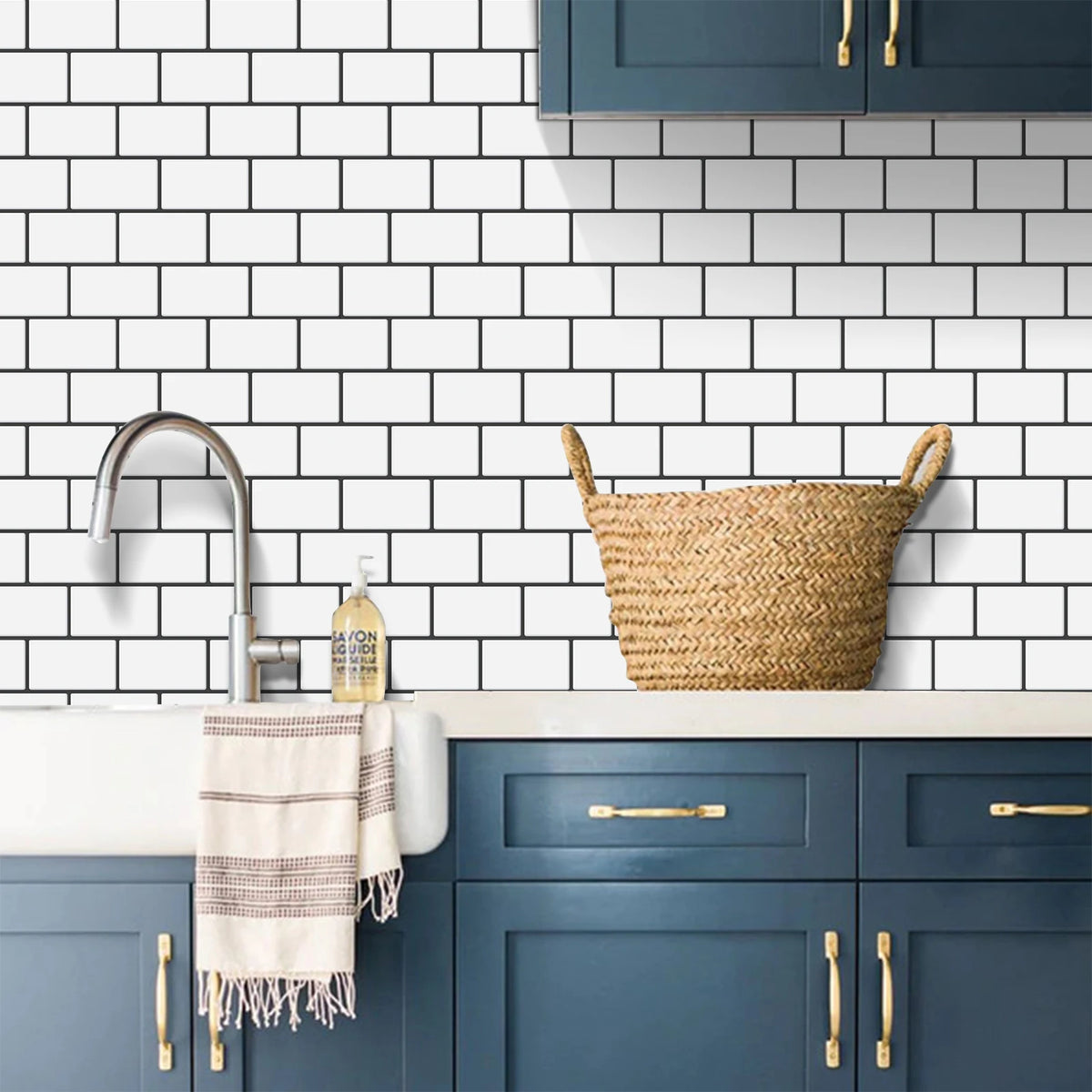A kitchen backsplash featuring white subway tiles, a sink, and dark blue cabinetry with gold hardware.