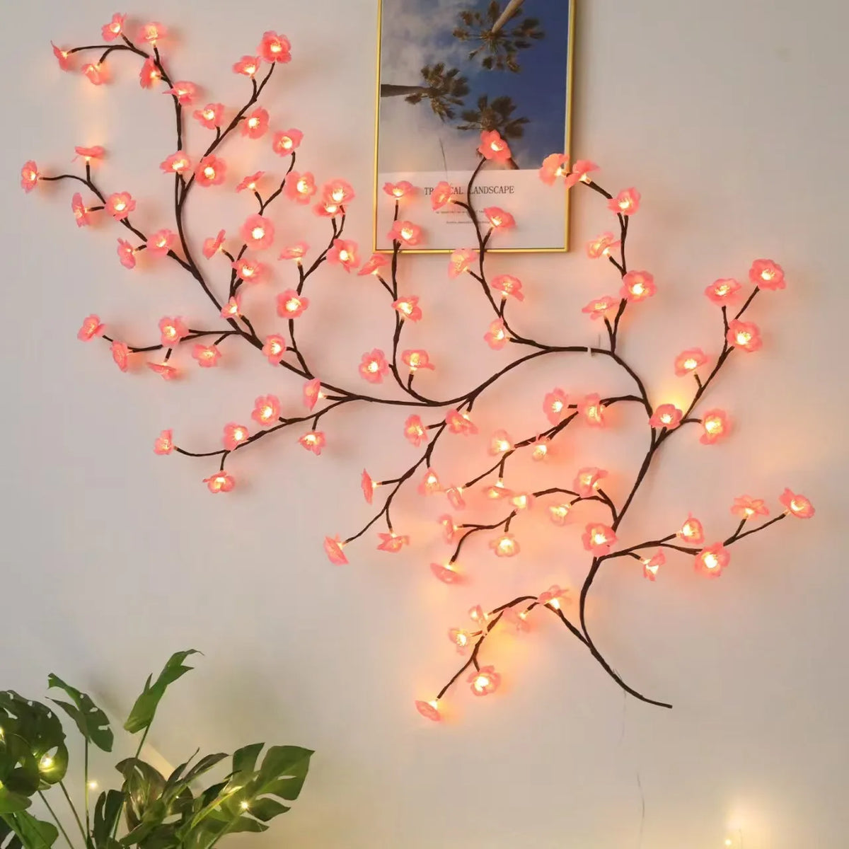String lights shaped like flower vines with pink cherry blossoms illuminating a framed picture.